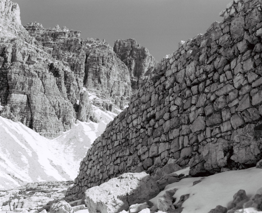 Blick auf eine Felswand gegenüber den Drei Zinnen (Dolomiten), im Vordergrund eine Mauer aus Bruchsteinen